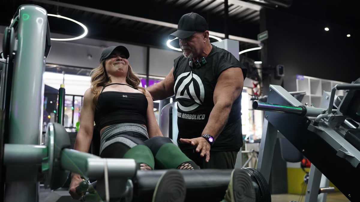 A personal trainer assists a woman with a leg press exercise in a modern gym setting.